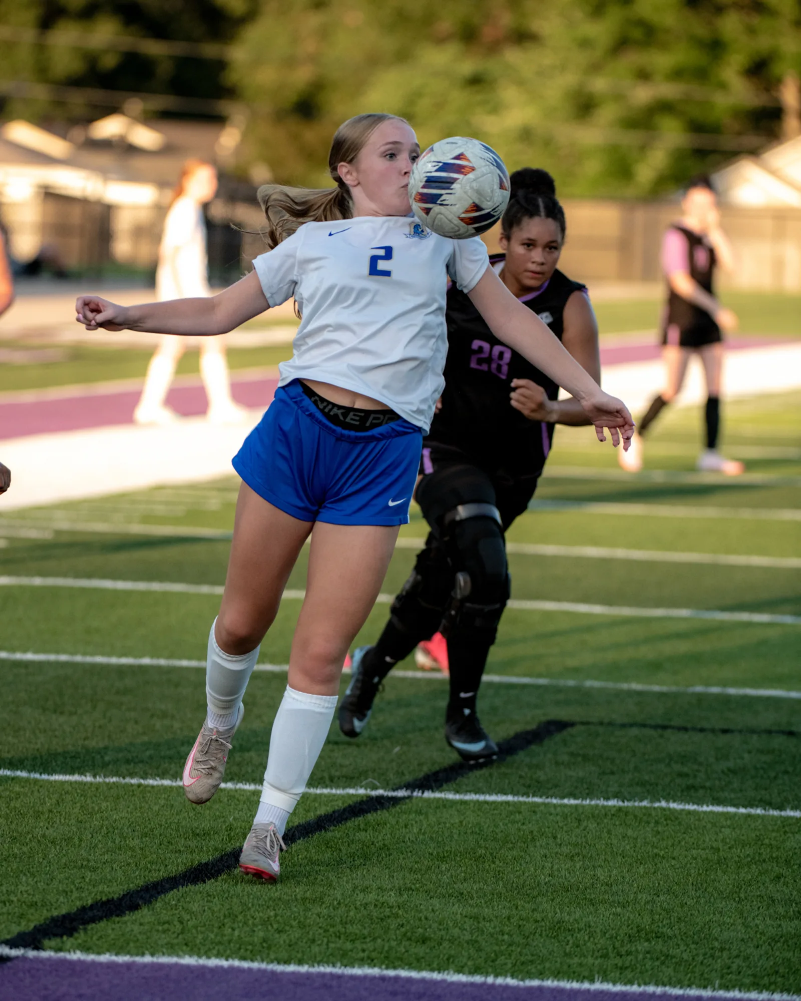 Girls soccer player chesting the ball down with a defender closing in behind her