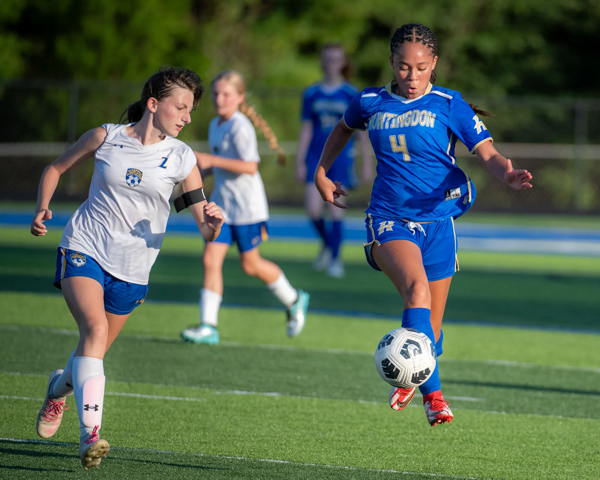 Girls soccer player in blue taking the ball forward while an opposing defender gives chase