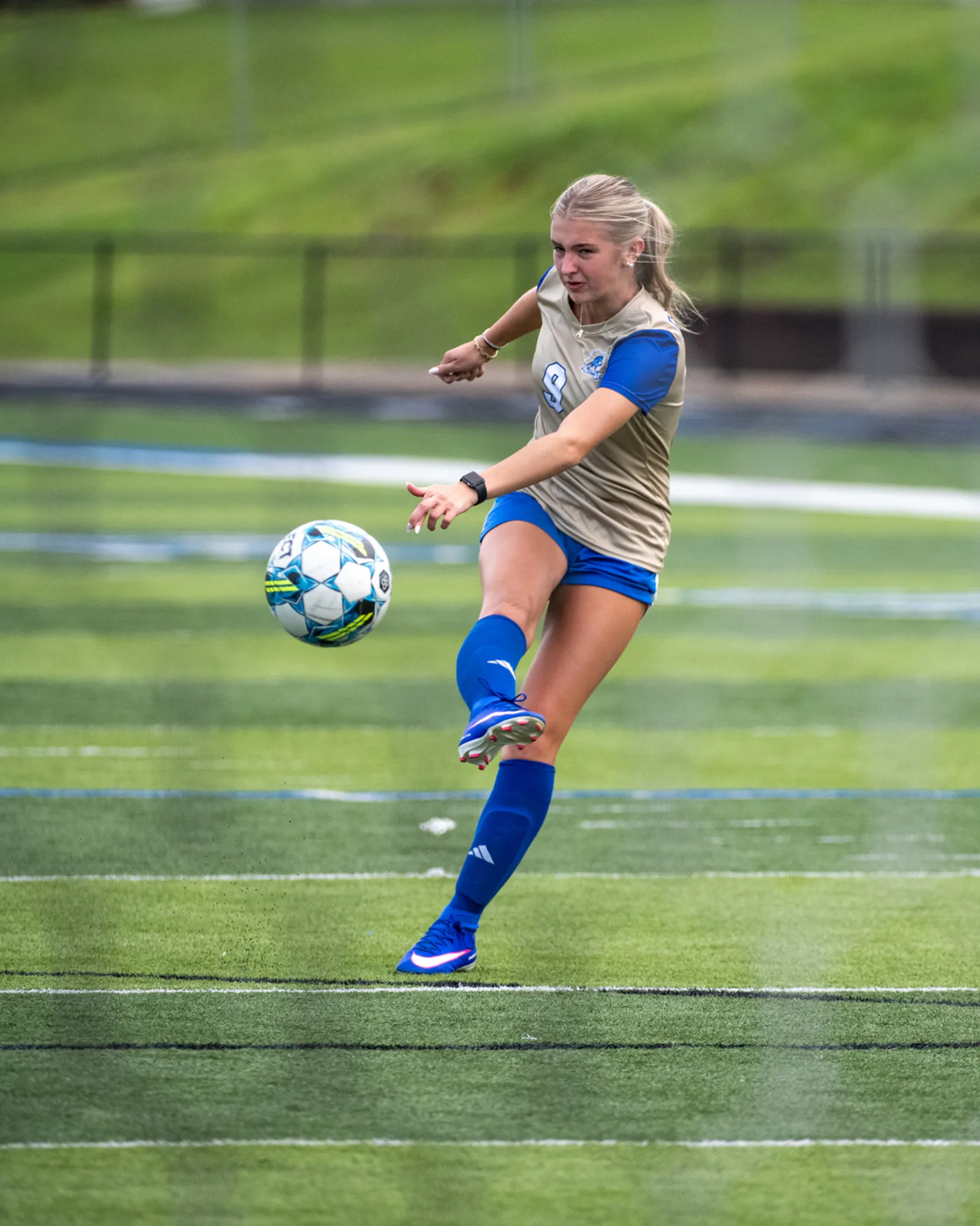 Girls soccer player driving the ball downfield in a tan and blue Huntingdon kit