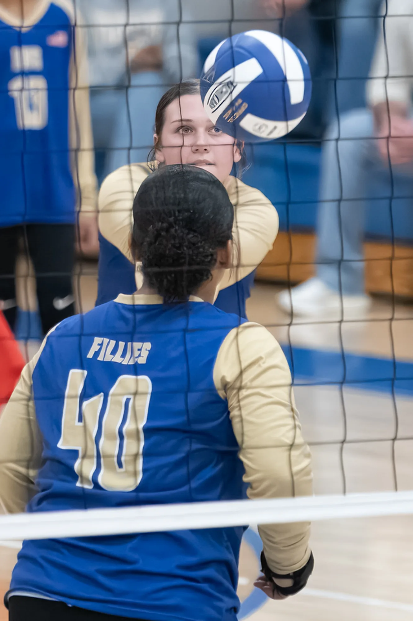 Volleyball players framed through the net as one passes the ball in a home gym