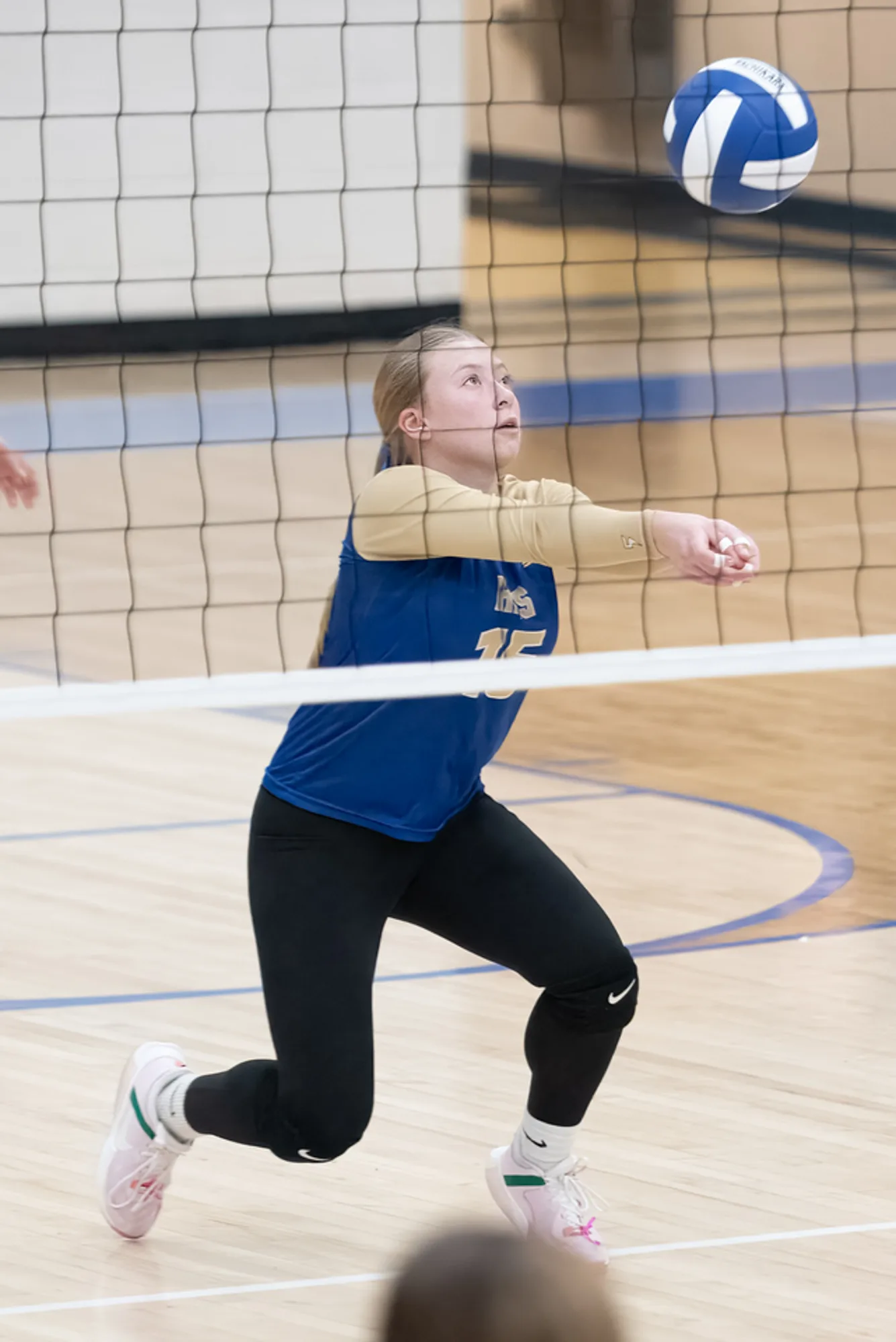 Volleyball player stepping into a forearm pass as the ball drops over the net