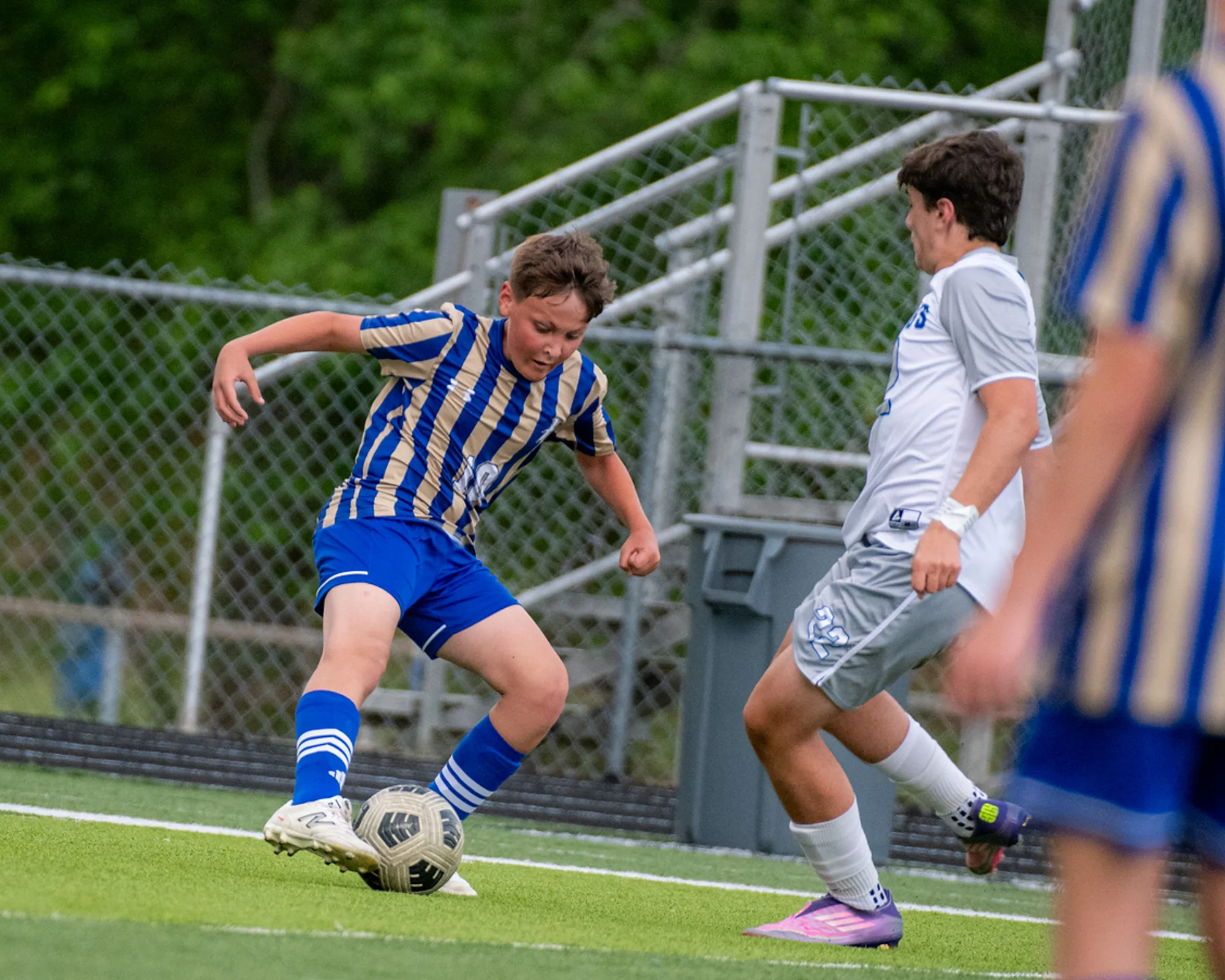 Boys soccer player in blue and gold stripes turning the ball away from a defender