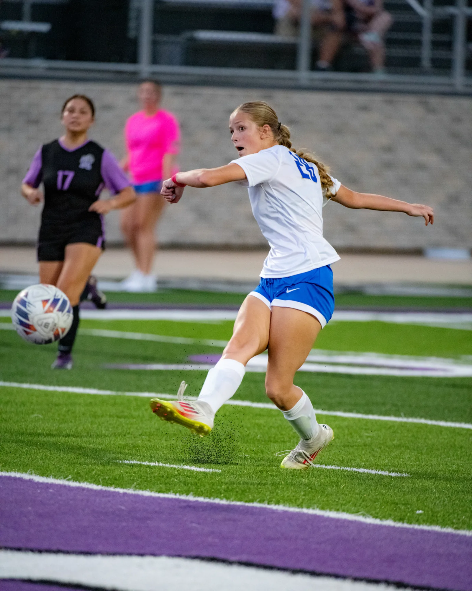 High school girls soccer player striking the ball under the lights at a night match